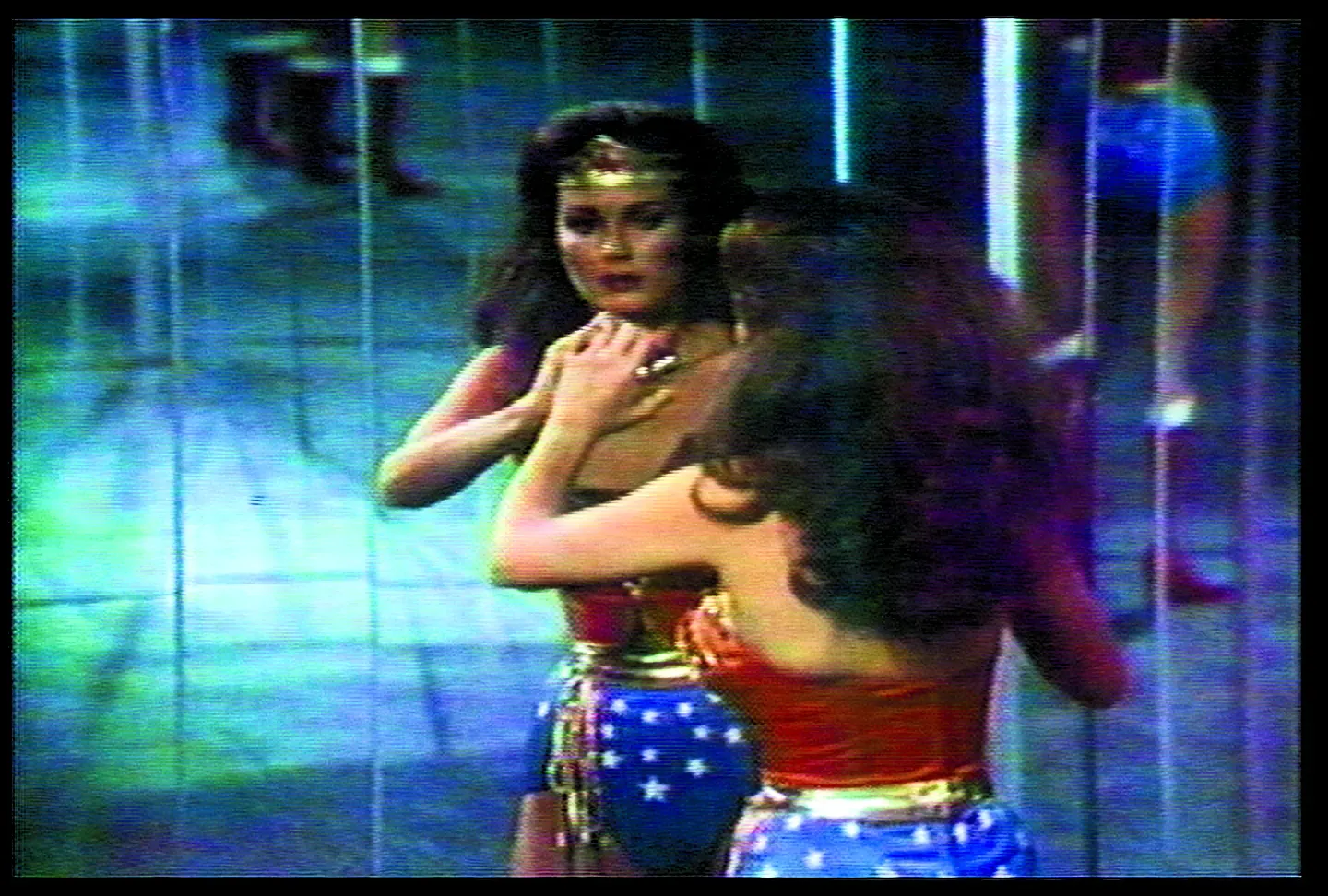 An image from the original Wonder Woman television series, with Wonder Woman looking at herself in a mirrored, lined surface.