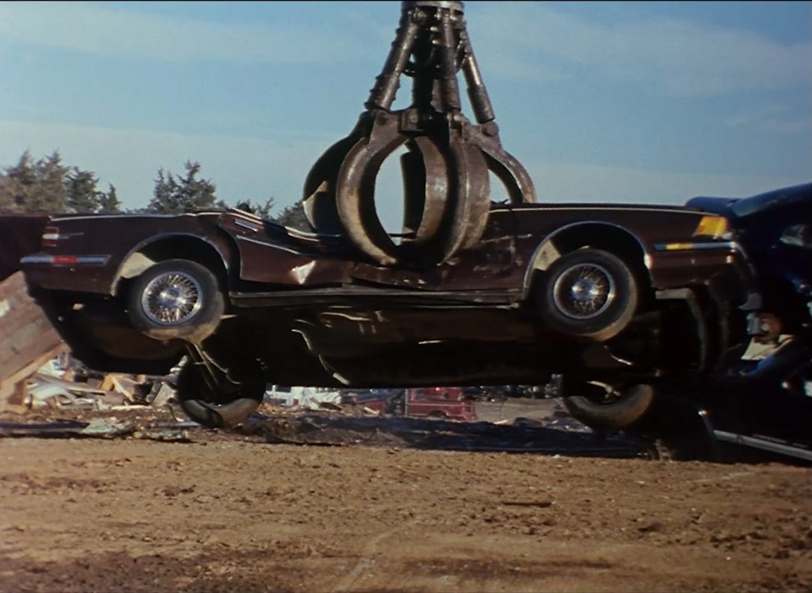 A car being crushed by a mechanical crane arm.