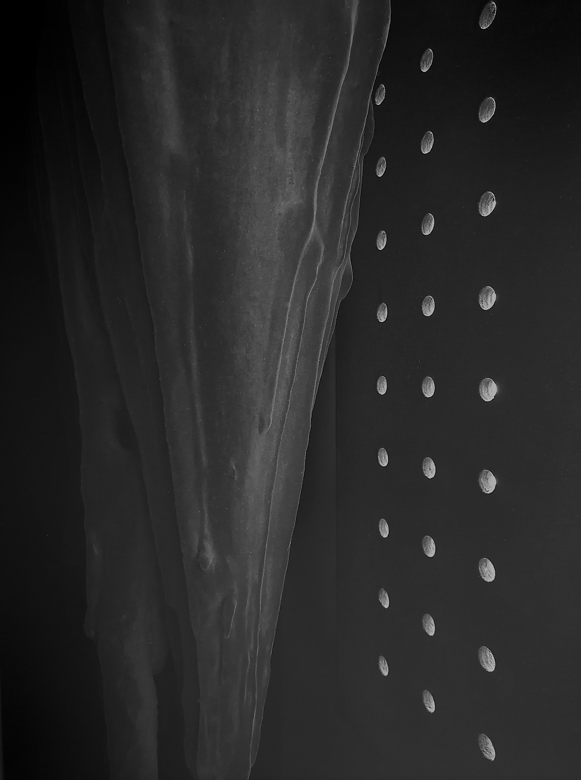 A dark gray, abstract sculpture encased in a box with a series of holes that allow light inside.