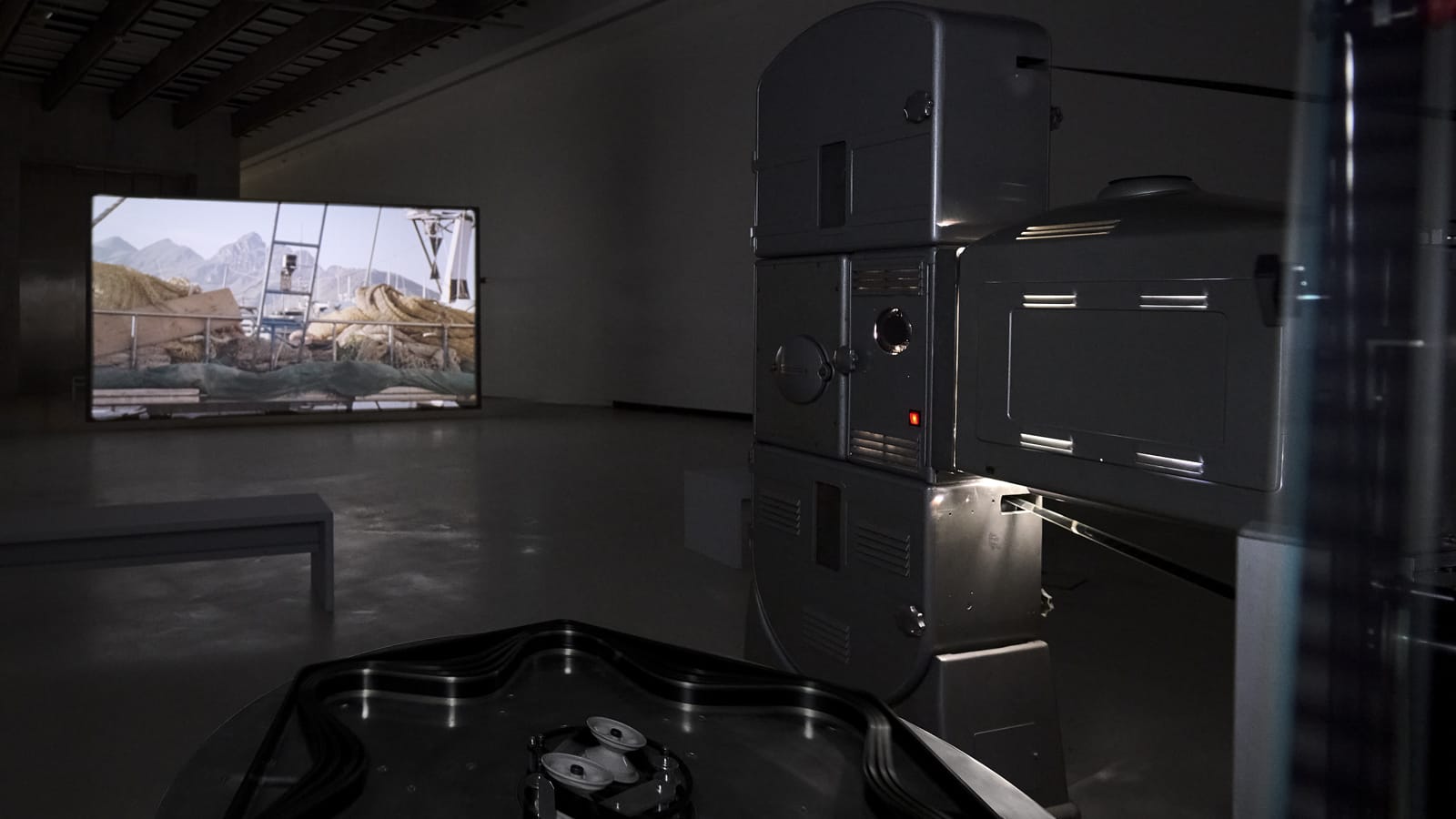 An installation view with a projector and celluloid film reels, with the projected image on a distant wall.