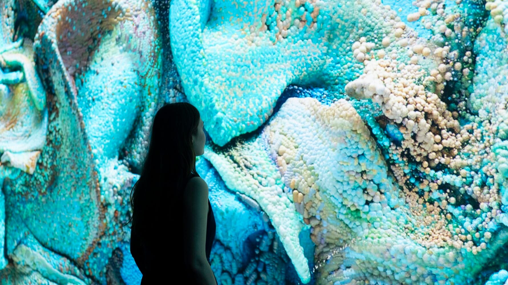 A woman in shadow standing in front of an immersive installation with swirling waves of color.