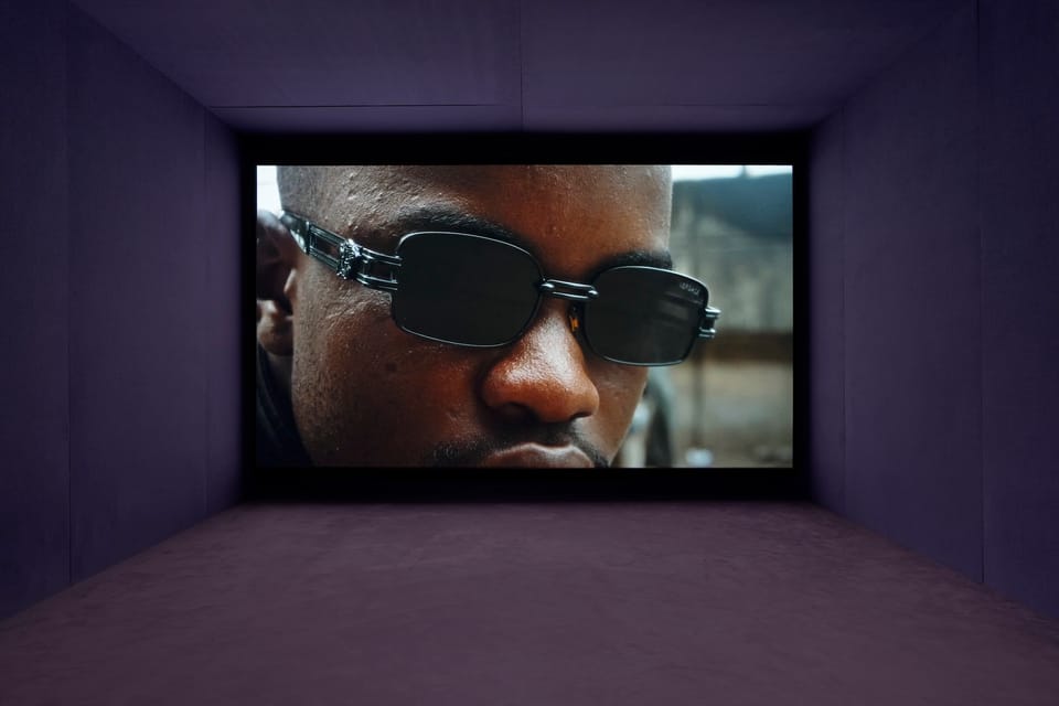 A large screen in a gallery with an image of a Black man wearing sunglasses.