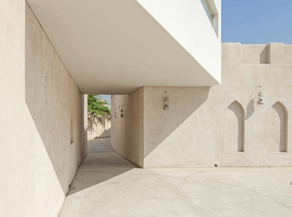 A pale, sandy-colored exterior architectural structure with lamps hanging on the walls.