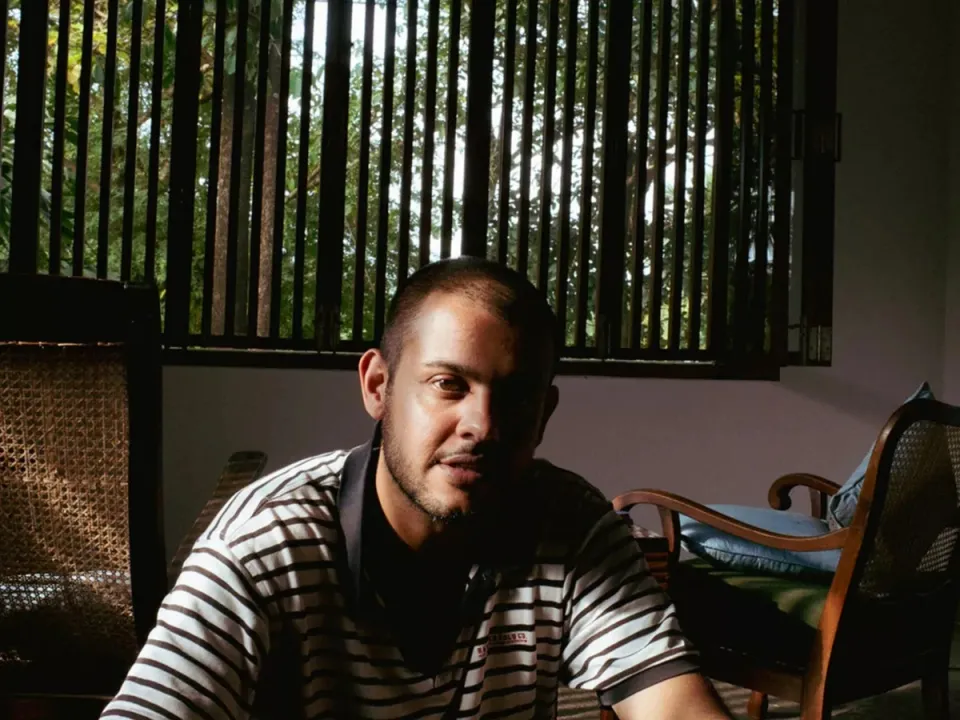 A man wearing a striped shirt, with half his face in shadows, glances at the photographer shooting him.