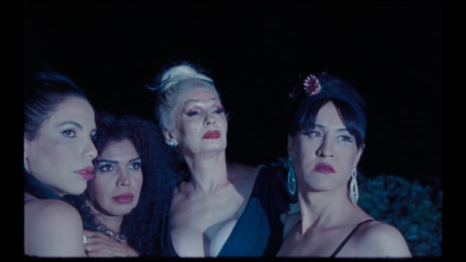 Four women against a black background, wearing heavy makeup and festive clothing, gazing off-frame with concerned expressions.