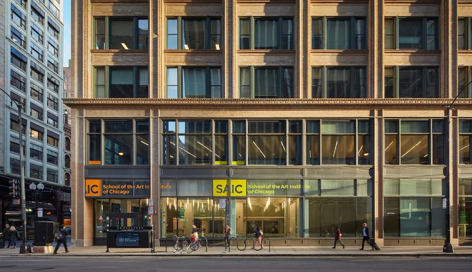 A large building with glass windows on a busy urban street, with the logo for School of the Art Institute of Chicago placed above the main entrance.