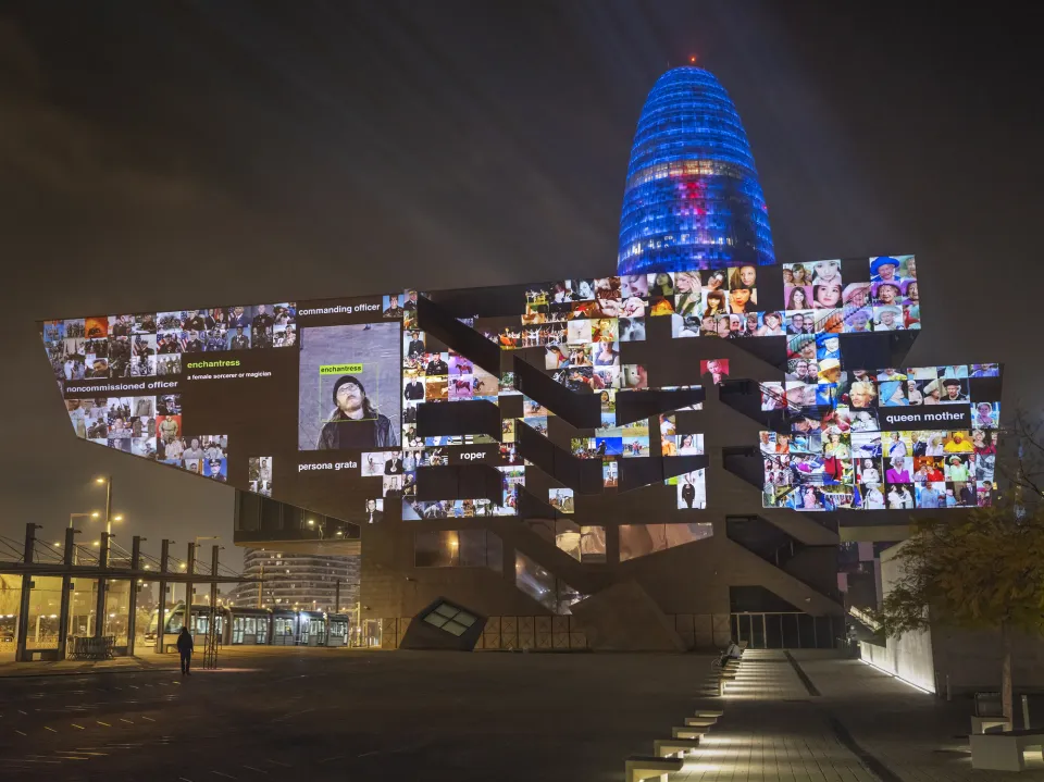 A modernist building at night with a collage of digital images generated by machine intelligence projected onto it.